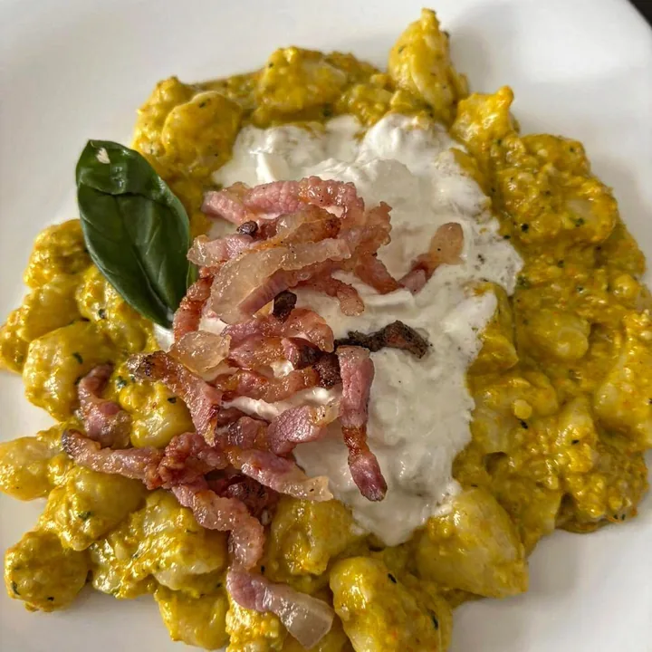 Gnocchi in una crema gialla con stracciatella, guanciale e una foglia di basilico.